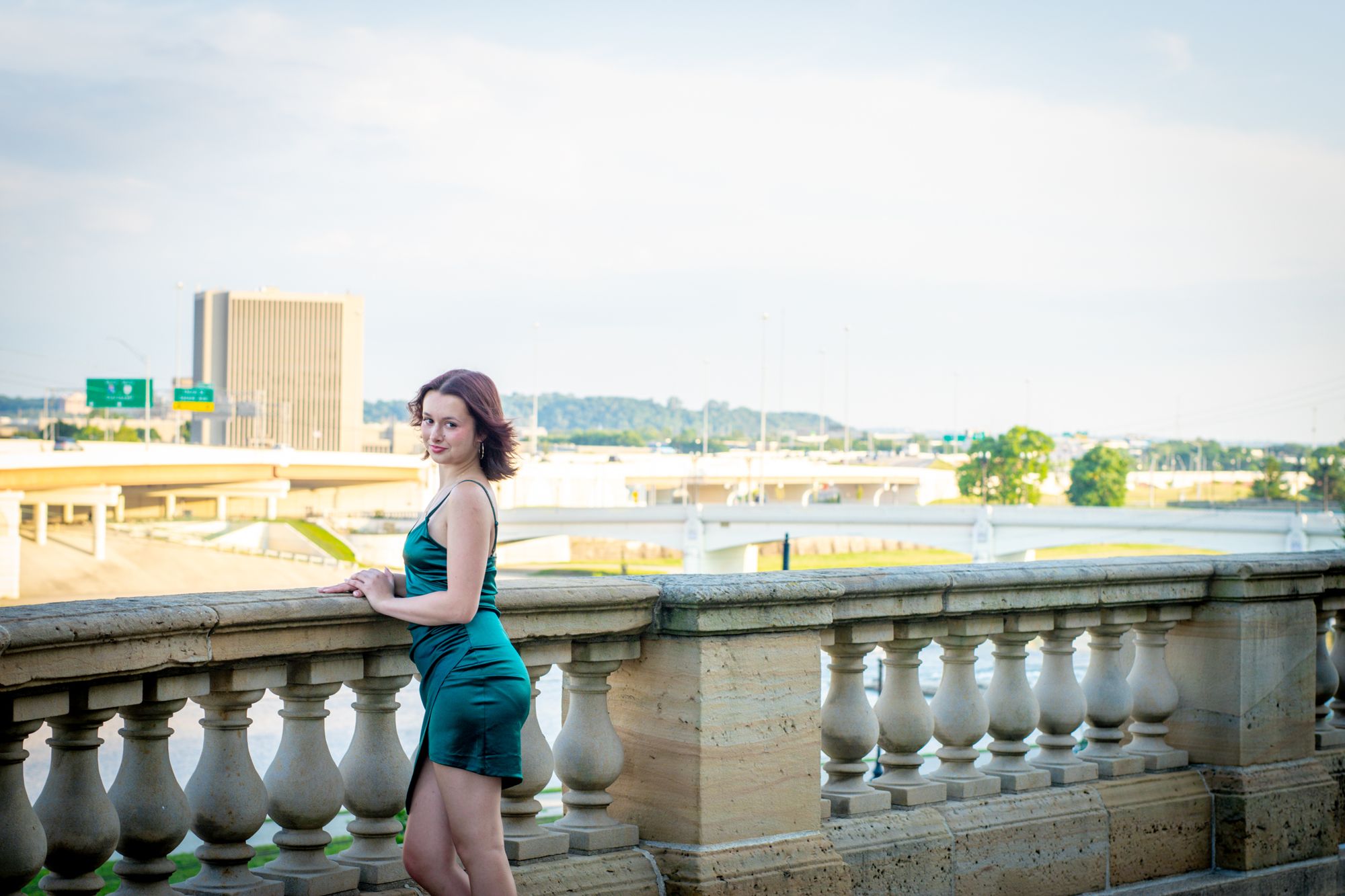A senior turning back toward the camera at a stone balustrade above the river, city buildings in the distance
