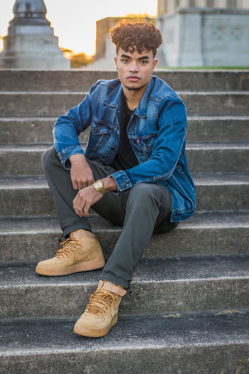 A high-school senior seated on wide stone steps at golden hour, stonework and warm light behind him