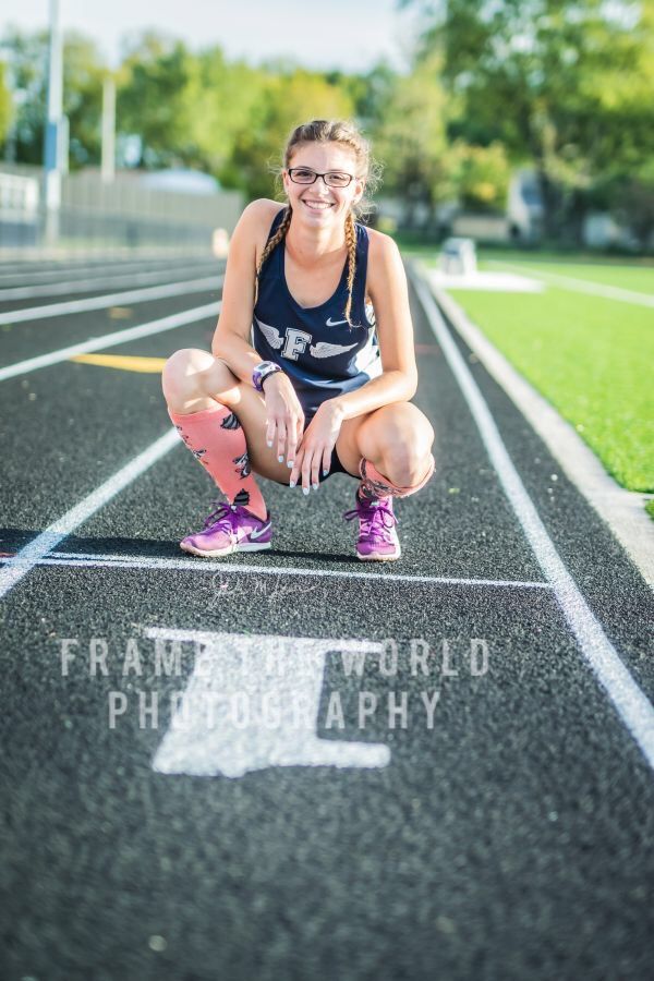 A high-school senior in track kit crouched on the lane markings of a school running track, smiling